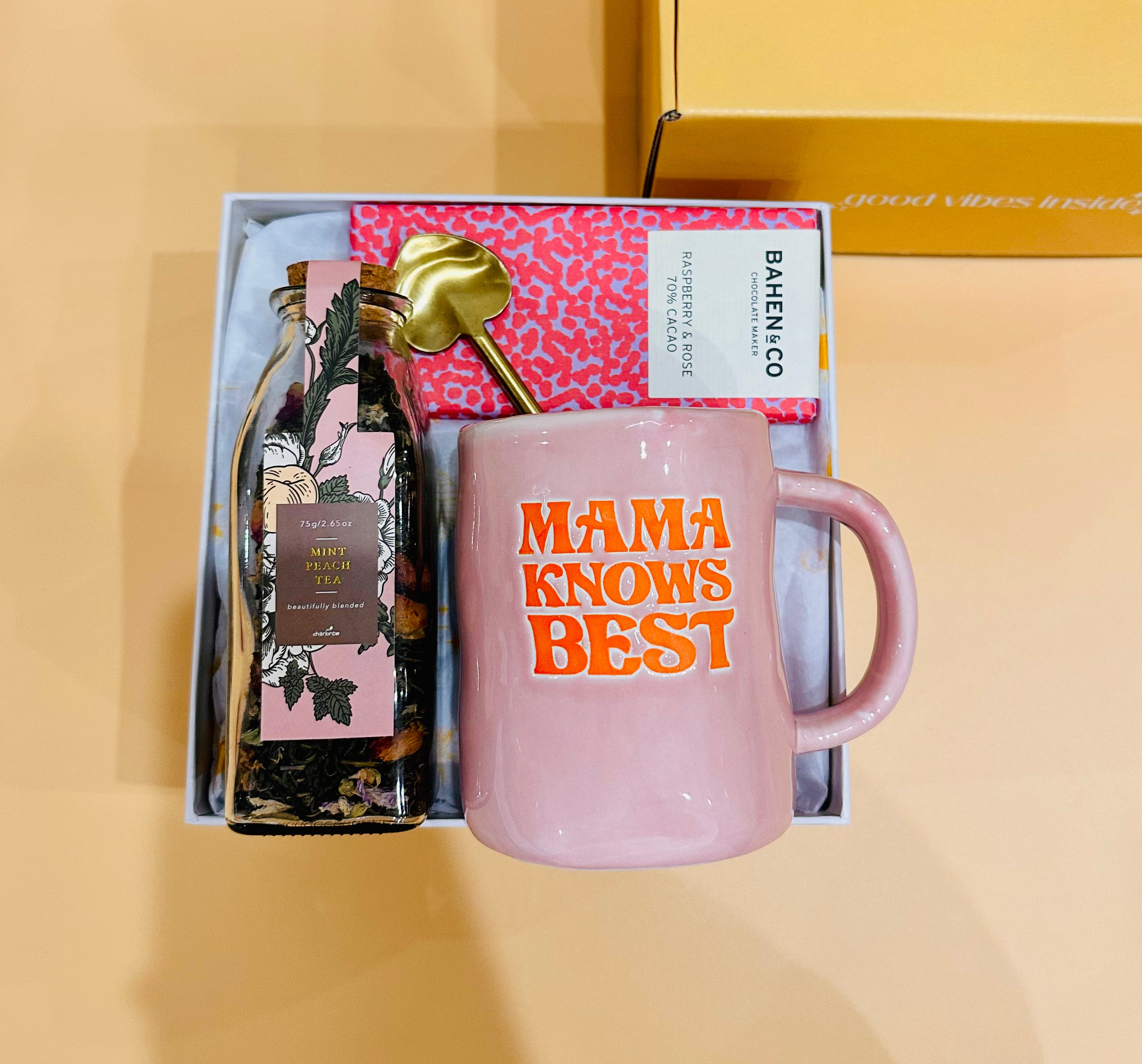 Large Mug with the words 'Mama knows best'  A Bahen and Co Raspberry flavour chocolate bar. A heart shaped gold spoon and some mint peach tea in a glass jar.